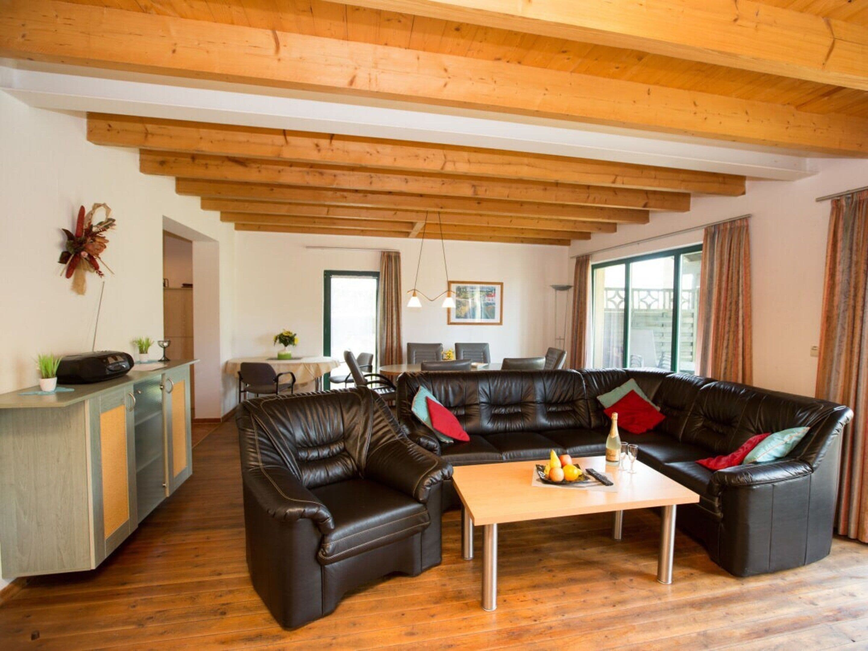 Un salon avec un plafond en bois, un ensemble de meubles pour le salon, un coin repas et un coin cuisine.