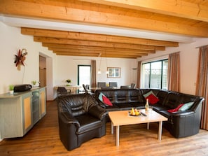 Ein Wohnzimmer mit Holzbalkendecke, einer Sofagarnitur, einem Essbereich und einer Küchenzeile.