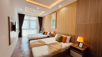 A hotel room with two beds, a TV mounted on the wall, a wooden panel wall, and a window with curtains.