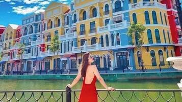 A woman in a red dress standing on a balcony with a view of colorful buildings and a river.