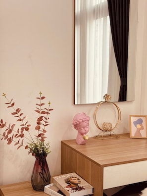 Ein hölzerner Schminktisch mit Spiegel, eine Vase mit getrockneten Blumen, eine rosafarbene Büste, ein goldrahmiger Spiegel und ein gerahmtes Bild.