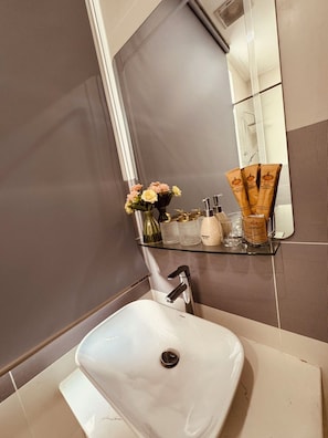 Ein Badezimmer mit einem weißen Waschbecken, einer Glasablage für Toilettenartikel und einem Spiegel über dem Waschbecken.