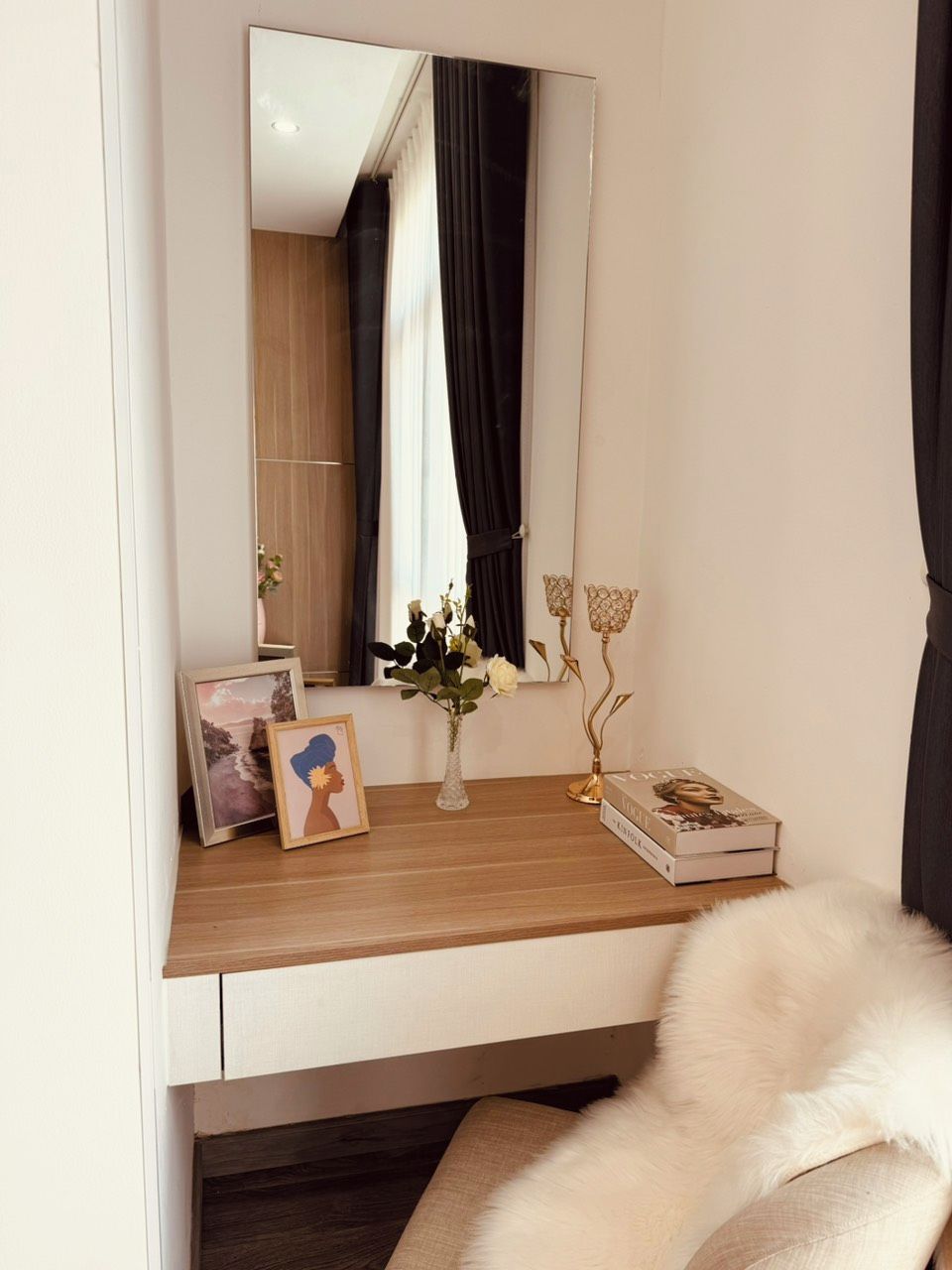 Une chambre à coucher avec une table de chevet en bois, un miroir, un tableau encadré, un vase avec des fleurs et un livre.