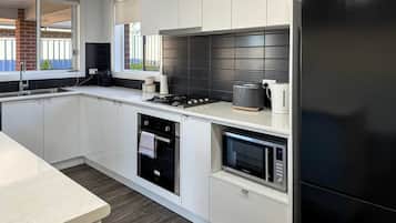 A modern kitchen with white cabinetry, a black refrigerator, a built-in oven, and a microwave.