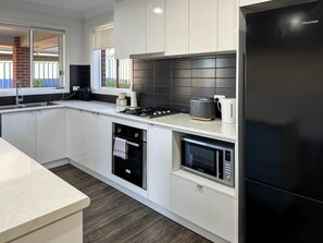 A modern kitchen with white cabinetry, a black refrigerator, a built-in oven, and a microwave. - St Pauls Comfort Home (Wagga Wagga)
