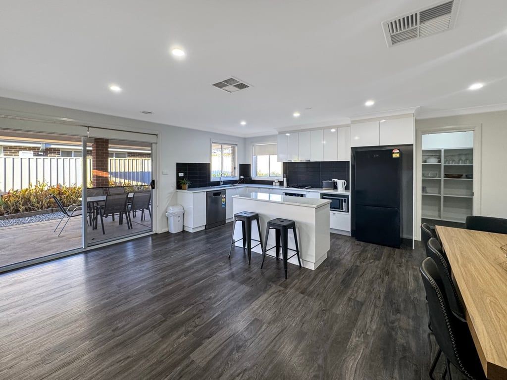 A modern kitchen with a central island, a dining area with a wooden table, and a sliding glass door leading to an outdoor patio.