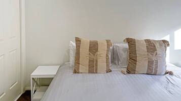 A bedroom with a bed, two pillows, a white nightstand, and a white wardrobe.