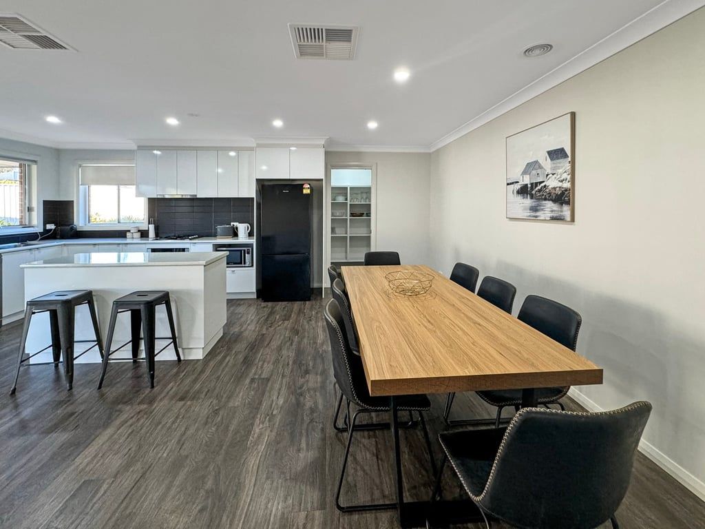 A modern kitchen with a central island, dining area with a wooden table and chairs, and a kitchen island with stools.