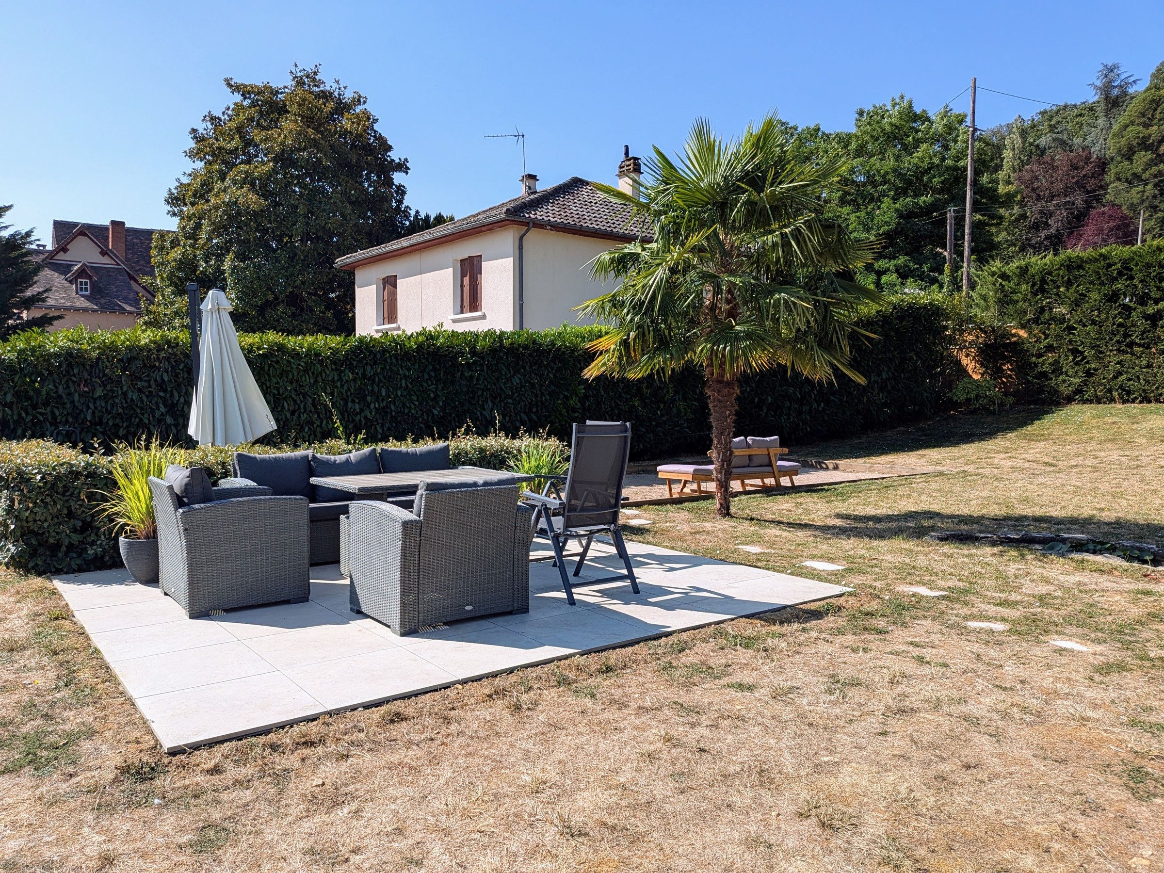 Un patio con mobiliario exterior, una palmera y un seto.