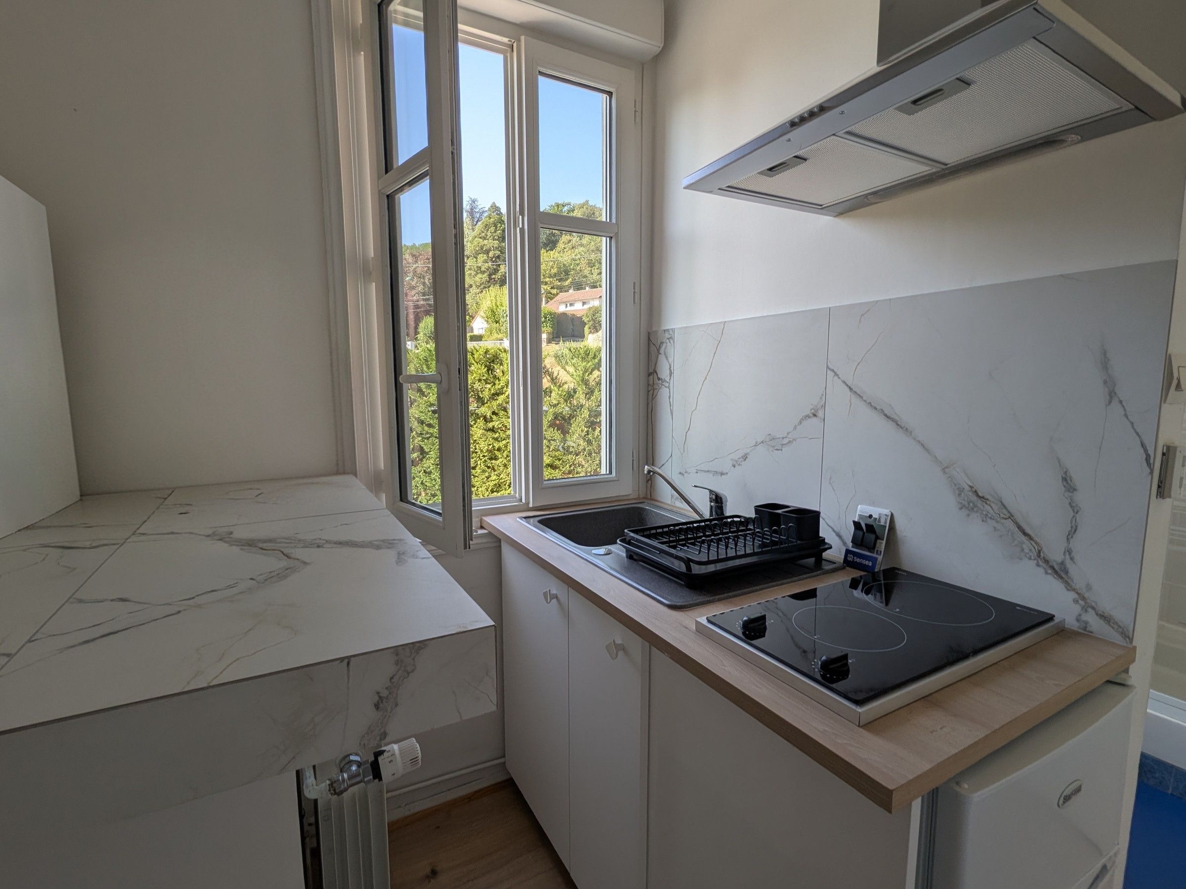 A kitchen with a built-in stove, a window with a view of greenery, and a marble backsplash.