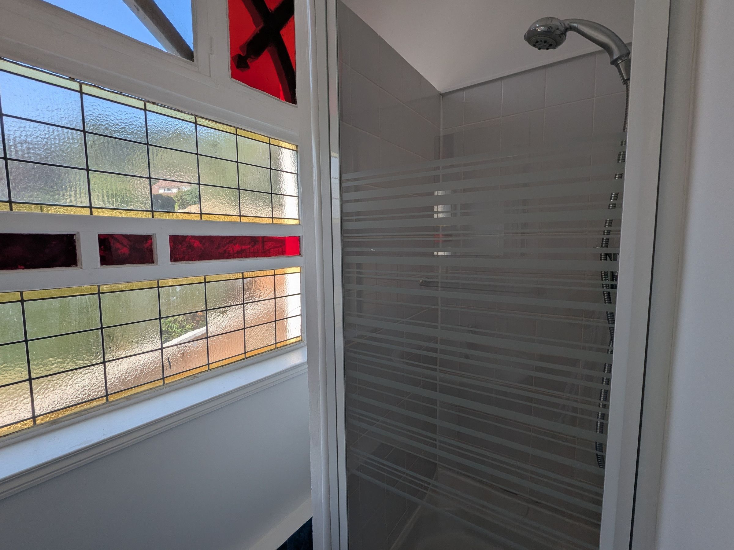 Une douche avec une porte en verre et une fenêtre ornée de vitraux.