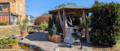 Un jardín con un pabellón, una parrilla y un estanque.