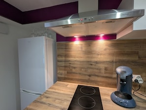 A kitchen with a modern design, featuring a stainless steel range hood, a built-in oven, and a coffee maker on the counter. - Charming studio with garden - 2 guests (Argenton-sur-Creuse)