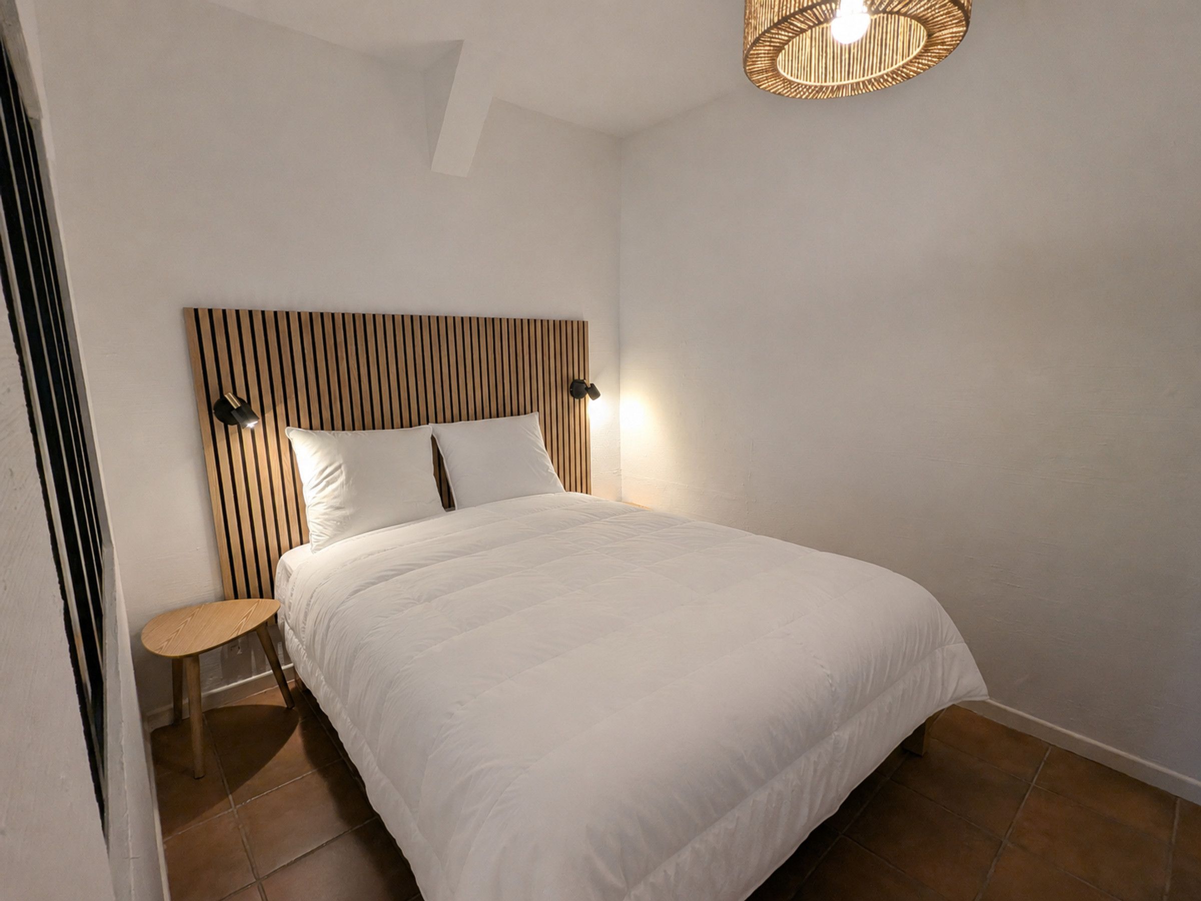 Een slaapkamer met een bed, een nachtkastje, een wandlamp en een plafondlamp.