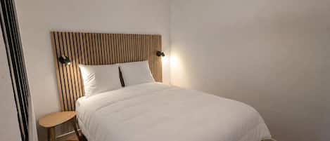 A bedroom with a bed, a nightstand, a wall-mounted lamp, and a ceiling light fixture.