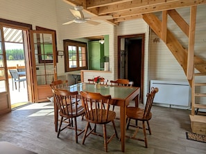A dining area with a glass-top table and wooden chairs, a ceiling fan, and a view of the outdoors. - Cozy chalet in nature - 6 guests (Ligny-le-Ribault)