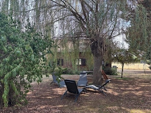 An outdoor seating area with two chairs and a table, surrounded by trees and a building in the background. - Cozy chalet in nature - 6 guests (Ligny-le-Ribault)
