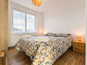 Un dormitorio con una cama grande, una mesita de noche con lámpara, un ventanal con vistas y suelo de madera.