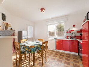Una cocina compacta con armarios rojos, una mesa de comedor con sillas y una ventana que proporciona luz natural.