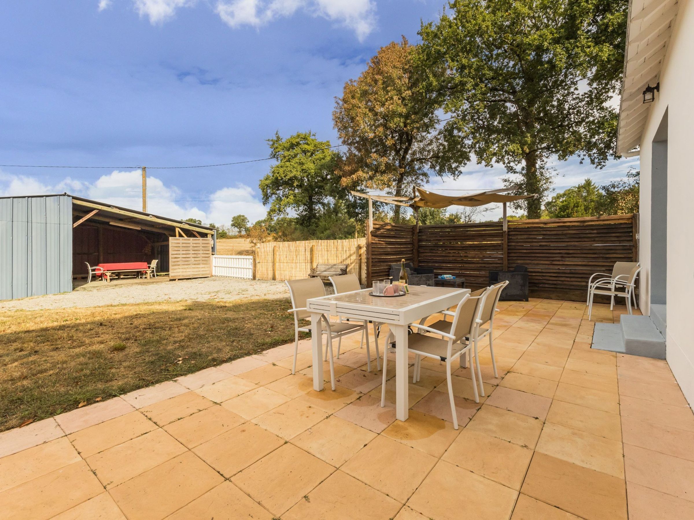 A patio with a table and chairs, a covered seating area, and a fenced yard with trees.