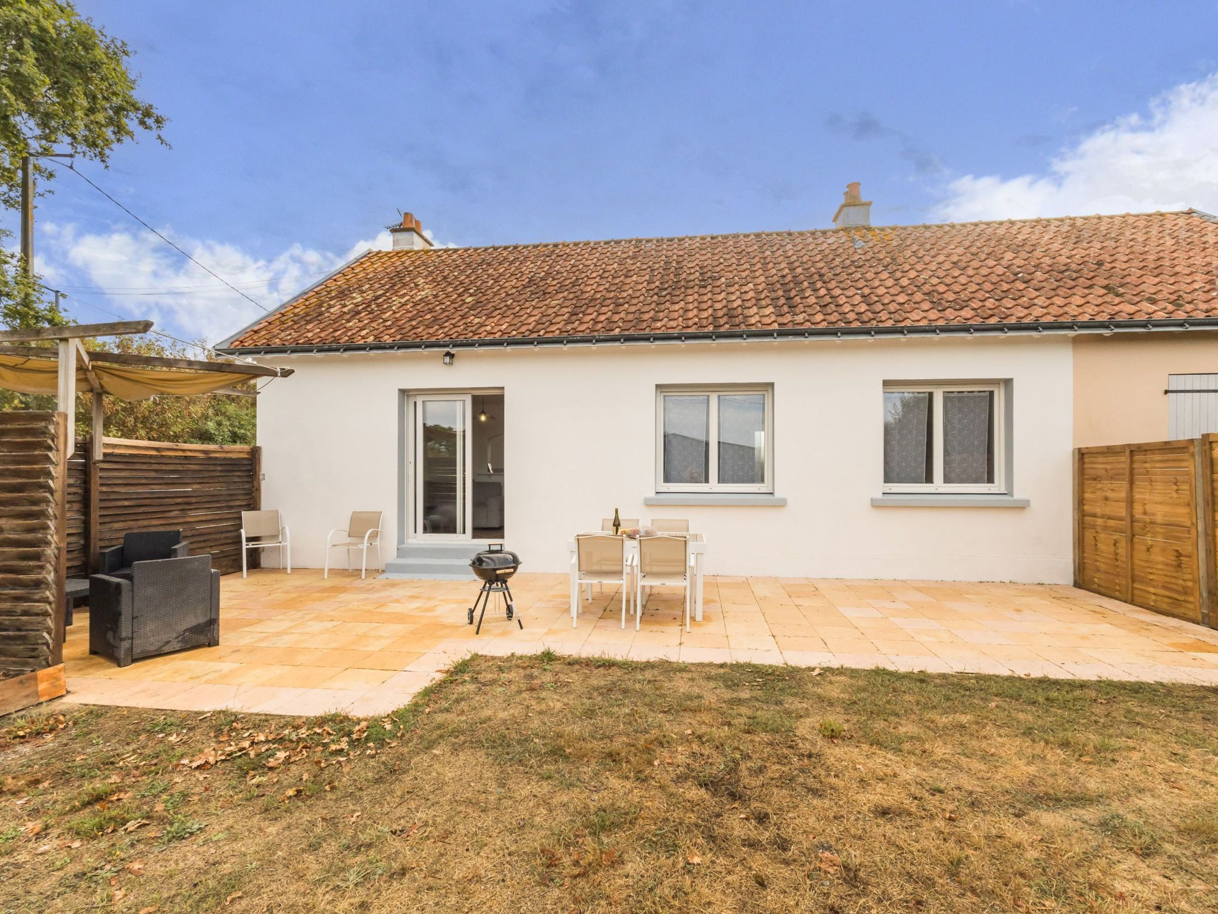 A single-story house with a tiled roof, a patio with outdoor furniture, and a grassy yard.