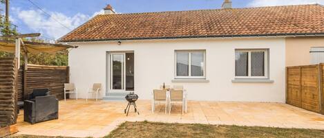 A single-story house with a tiled roof, a patio with outdoor furniture, and a grassy yard.