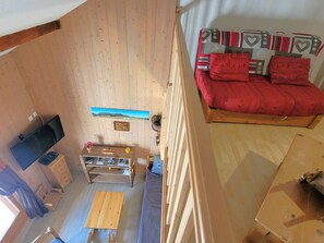 A room with a wooden floor, a red sofa, a television, a small wooden table, and a picture frame on the wall.