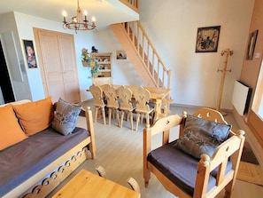 A cozy living room with a sofa, chairs, a dining table, and a staircase.