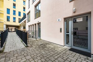 Un edificio con ingresso tramite porta in vetro, un cancello metallico e un vialetto lastricato che conduce a una scala.