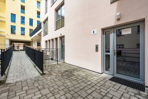 Ein Gebäude mit einem gepflasterten Weg, einem Glastür-Eingang und einem Schild mit dem Buchstaben 'E'.