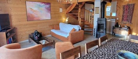 Ein gemütliches Holzinnere mit einer Couch, Sesseln, einem Kamin und einer Treppe.
