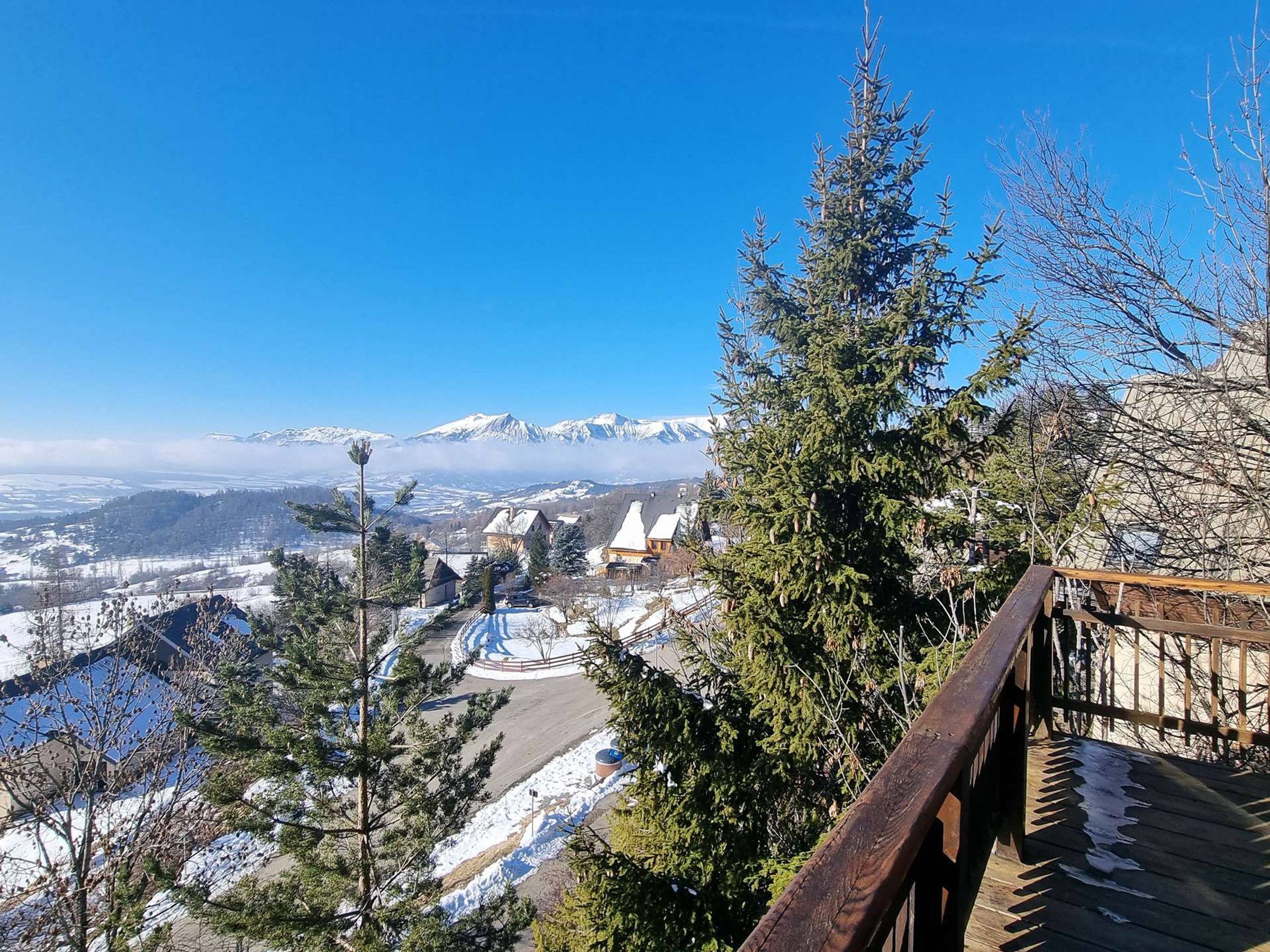 A panoramic view of a mountainous area with snow-covered landscapes, a wooden deck, and buildings in the background.