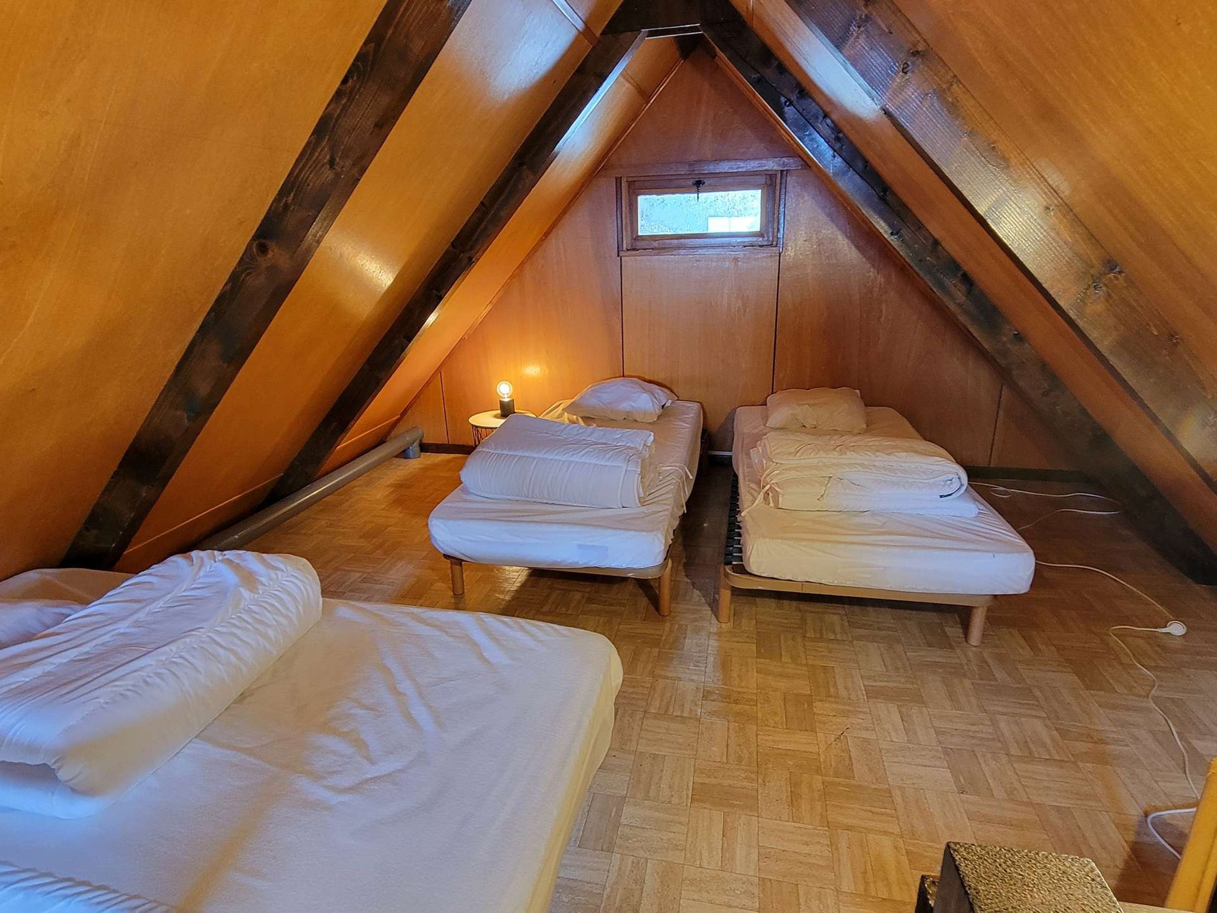 Un espacio ático pequeño y acogedor con dos camas, una ventana y una mesita de noche con lámpara.
