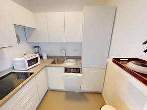 Cocina compacta con gabinetes blancos, microondas, pileta y estufa.