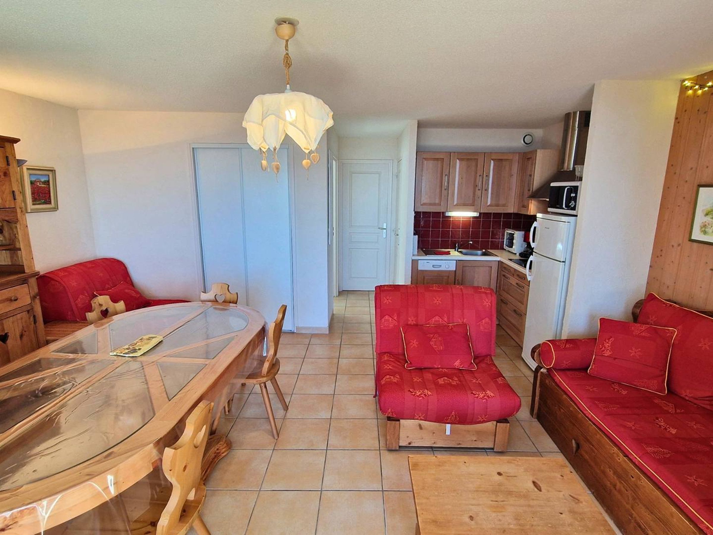 Een compacte keuken met houten kastjes, een eettafel met stoelen, een bank en een hanglamp.