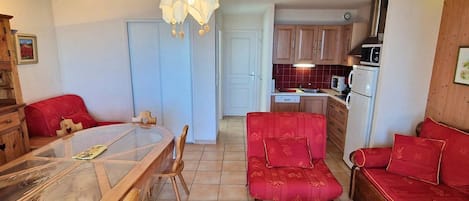 Eine kompakte Küche mit Holzschränken, einem Esstisch mit Stühlen, einer Couch und einer Pendelleuchte.