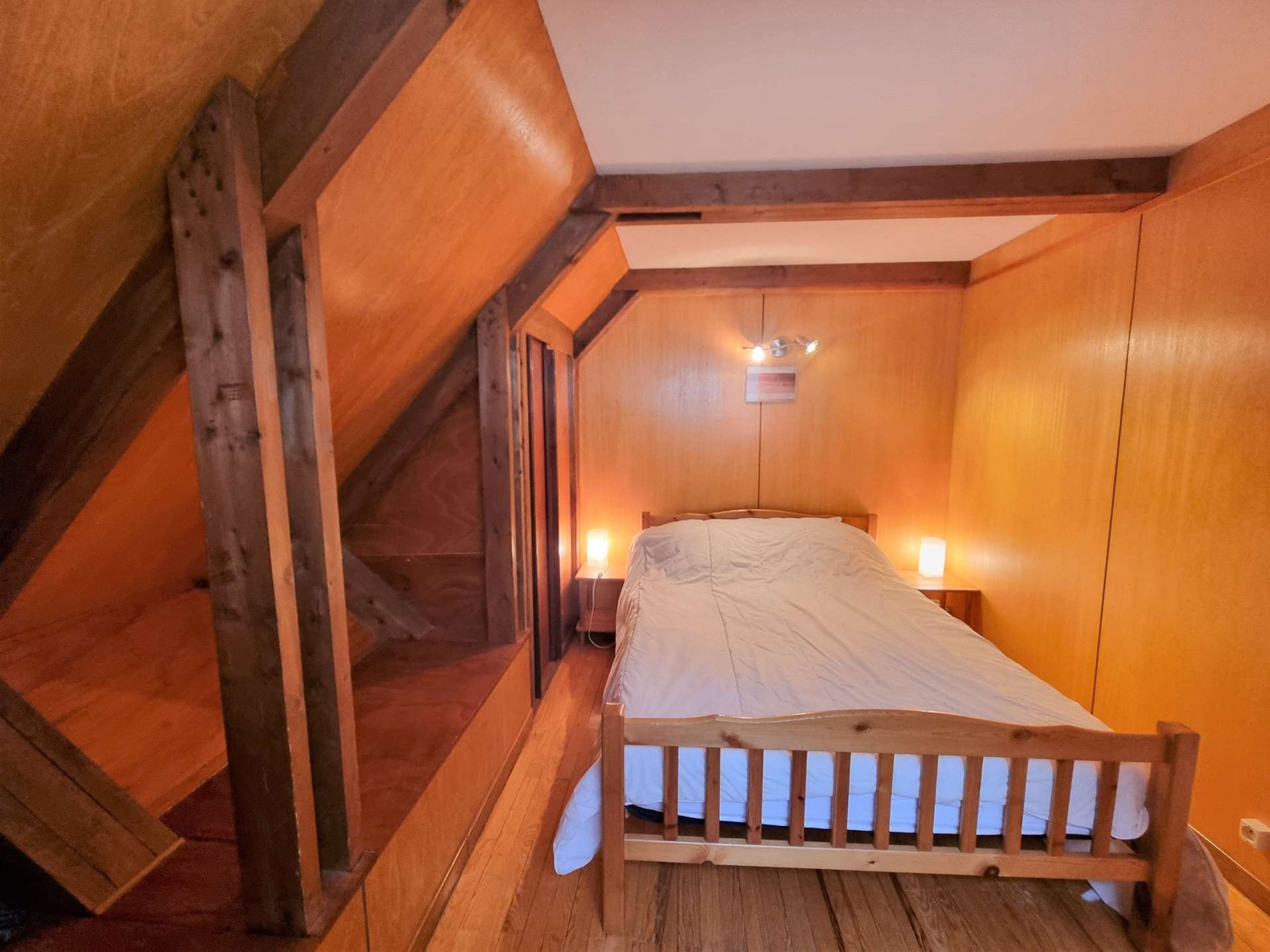 Una camera da letto mansardata accogliente, con un letto di legno, soffitto a falde e illuminazione calda.