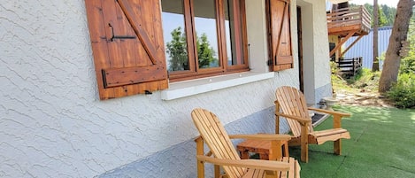 A building with wooden shutters, a window, and two wooden chairs on a green surface.