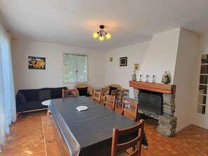 A dining area with a long table, chairs, a fireplace, and a sofa.