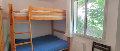 Ein Schlafsaal mit Etagenbetten, einem Fenster, Holzboden und einem Stuhl.