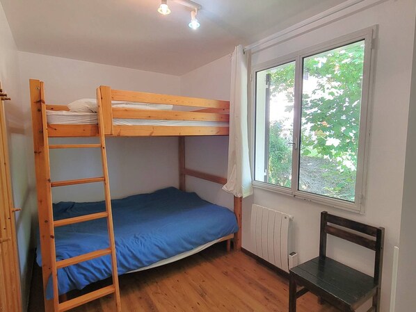 A bunk bed room with a window, wooden floor, and a chair.