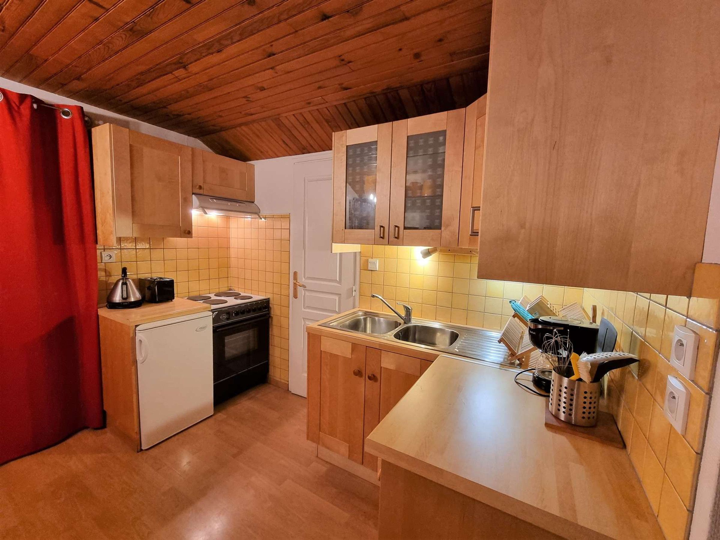 A compact kitchen with wooden cabinets, a stove, a sink, and a small refrigerator.