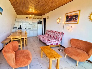 A compact living space with a wooden ceiling, a kitchenette, a dining area, and a sofa.