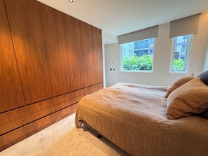 A bedroom with a large wardrobe, a bed with a beige bedspread, and two windows with a view of greenery. - Luxary apartment in downtown Reykjavik (Reykjavík)