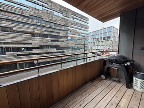 A balcony with a wooden floor, a grill, and a view of modern buildings. - Luxary apartment in downtown Reykjavik (Reykjavík)