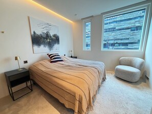 A bedroom with a large bed, a nightstand, a chair, and two windows. - Luxary apartment in downtown Reykjavik (Reykjavík)
