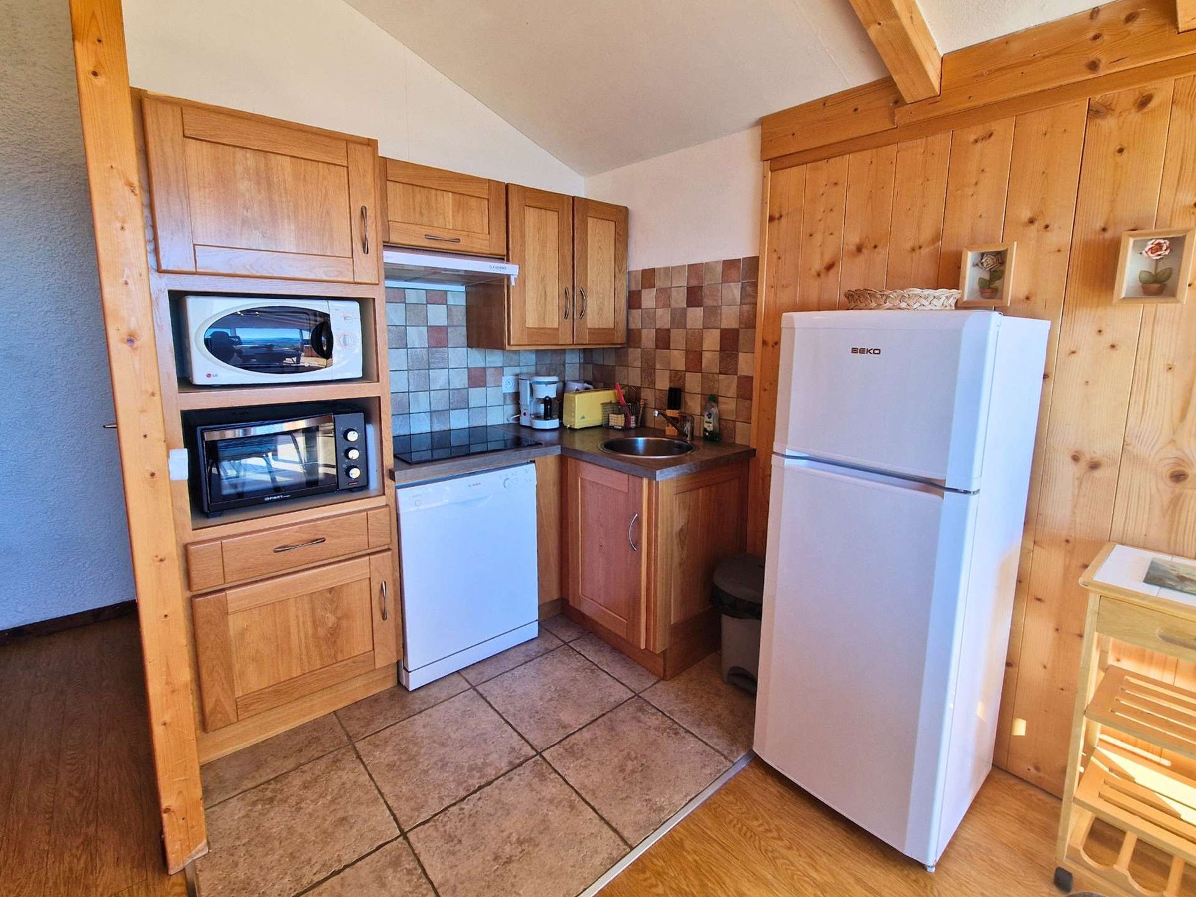 Une cuisine de taille réduite, dotée de meubles de rangement en bois, d’un four à micro-ondes, d’un lave-vaisselle et d’un réfrigérateur.