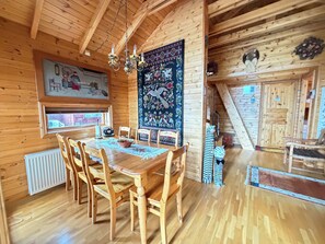 Ein Holzinterieur mit einem Esstisch, Stühlen, einer Kandelaber, einem Wandteppich und Blick ins Freie.