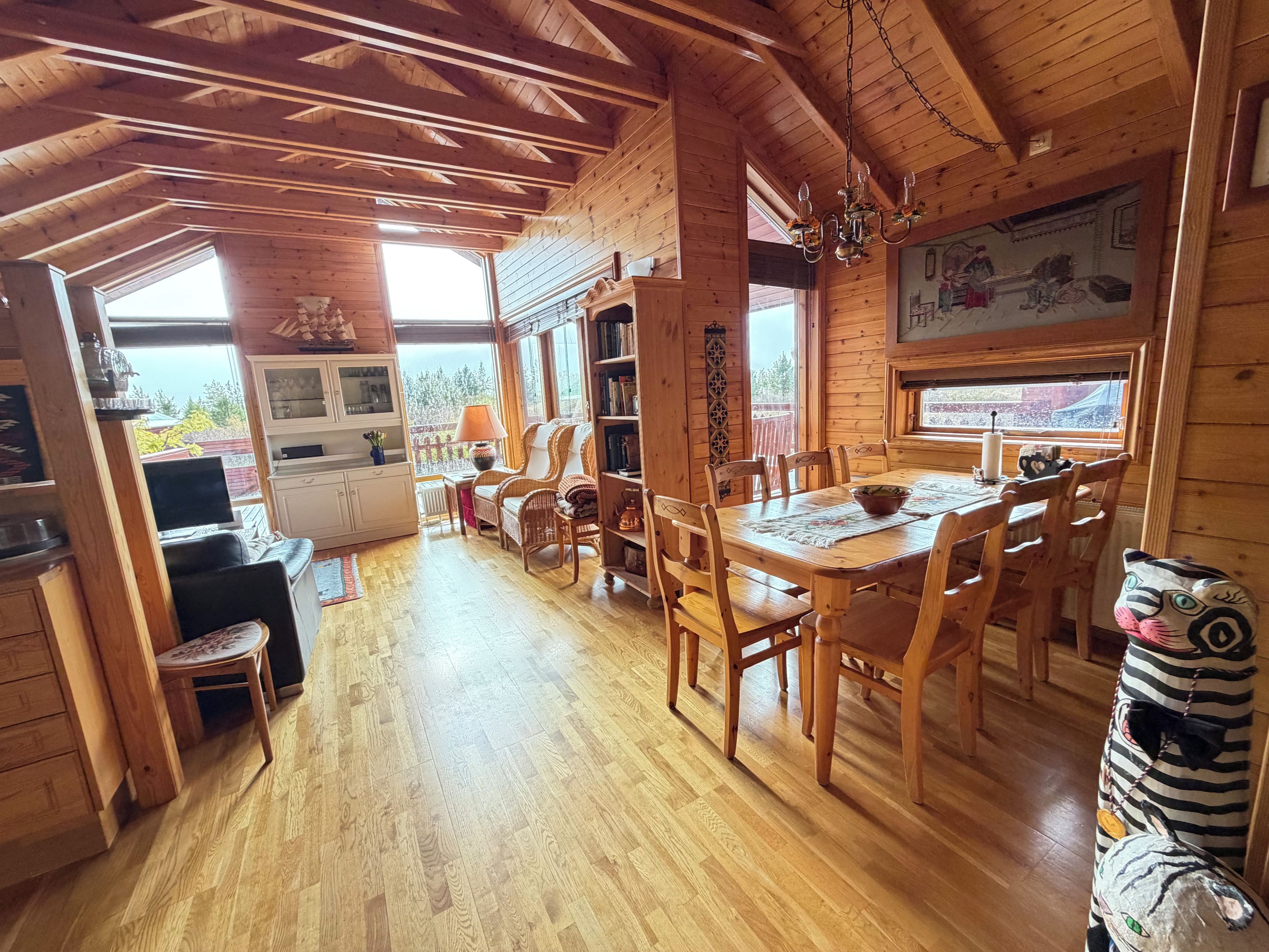 Ein Interieur einer Holzhütte mit Essbereich, Bücherregalen und Blick durch die Fenster.