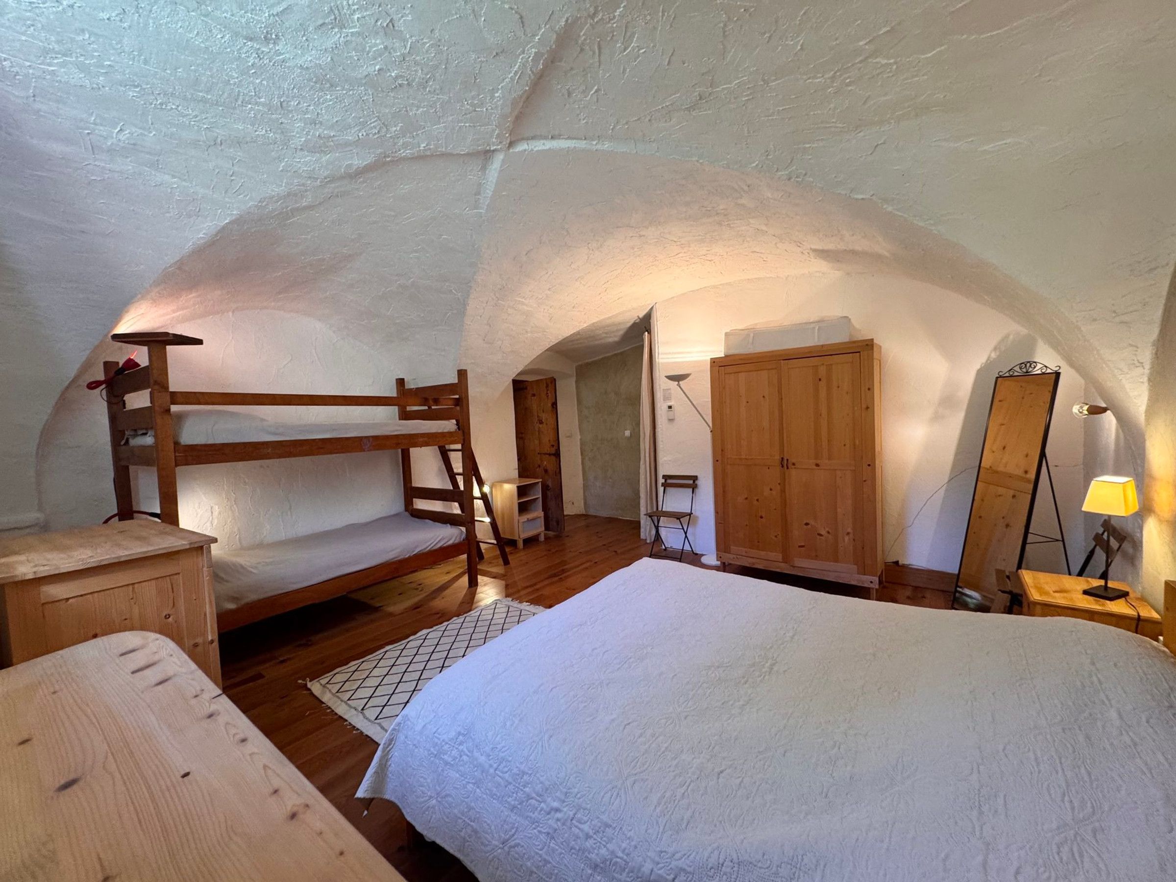 Ein gemütliches Schlafzimmer im Dachgeschoss mit Etagenbett, Holzschrank und großem Spiegel.